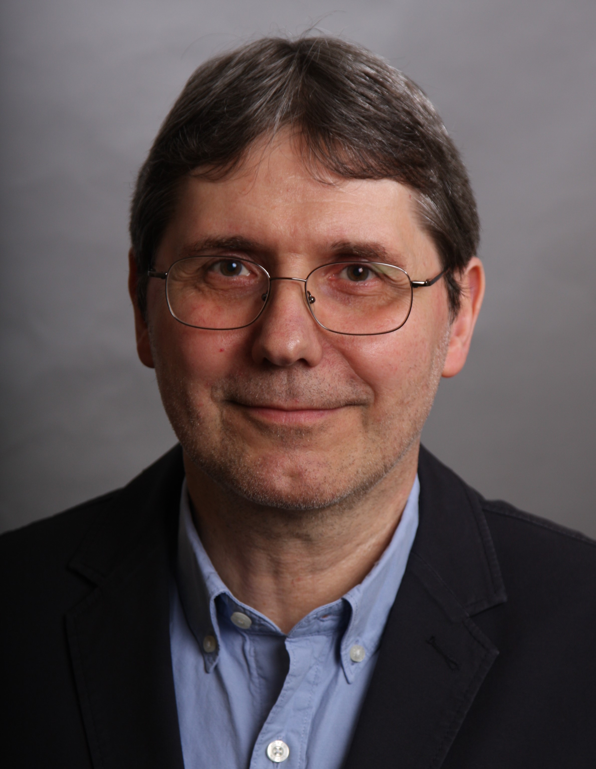 Andreas Koenig with glasses poses in front of grey background