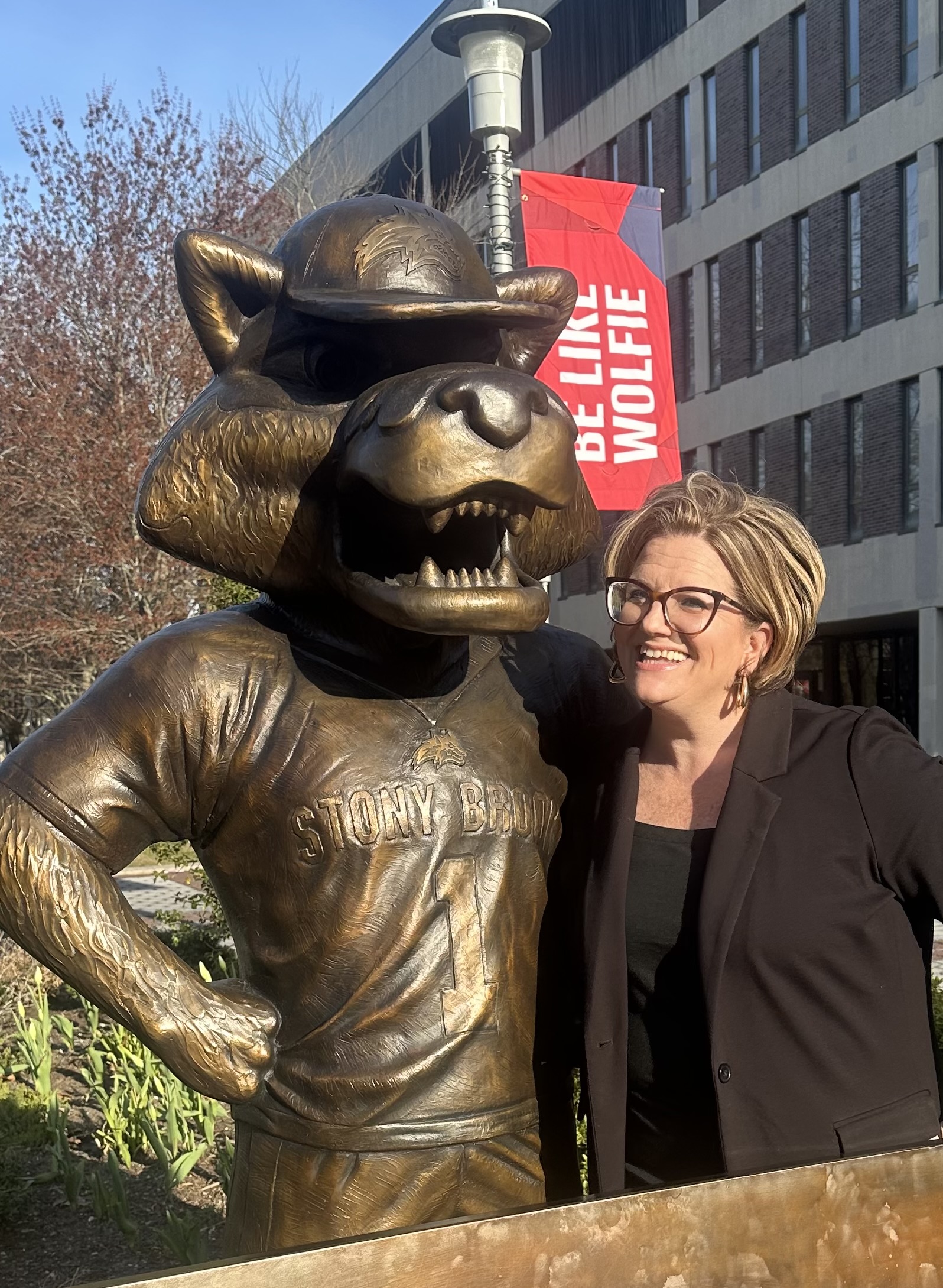 A person smiling next to the Stony Brook University Wolfie mascot statue.