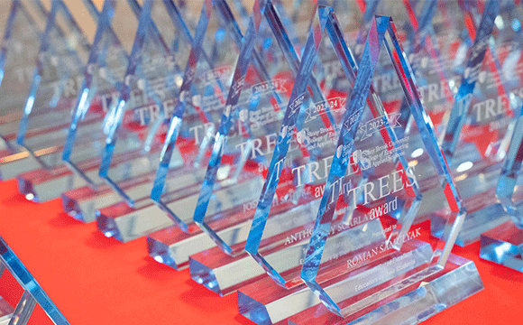 A row of transparent, blue-tinted glass awards shaped like elongated diamonds stand on a vivid red tablecloth, conveying a sense of celebration and achievement.