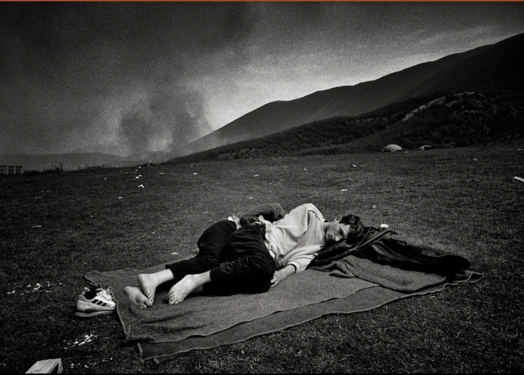 picture of two people sleeping in the grass, barefoot and on a blanket. The picture is grayscale, lifeless, and dull, and there is smoke rising in the background