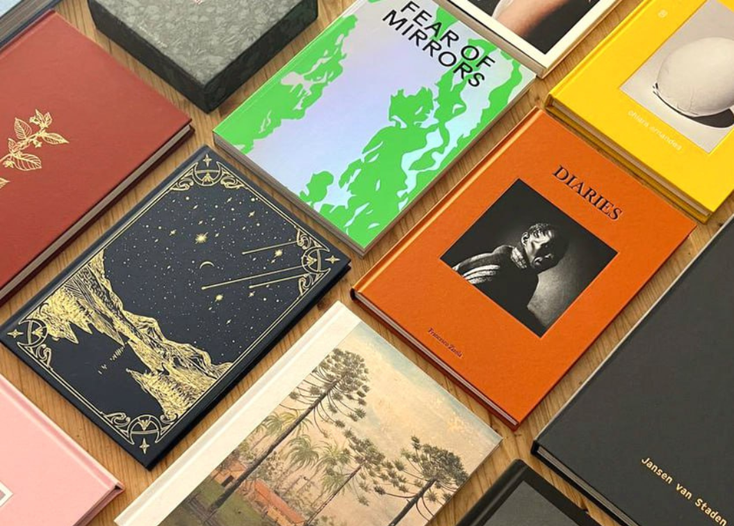 picture of a table with several multi-colored books; one is orange and titled "Diaries" and another is green and titled "Fear of Mirrors"