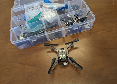 Micro quadcopter next to a box of parts
