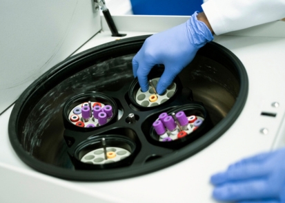 A gloved hand placing a test tube into a centrifuge machine